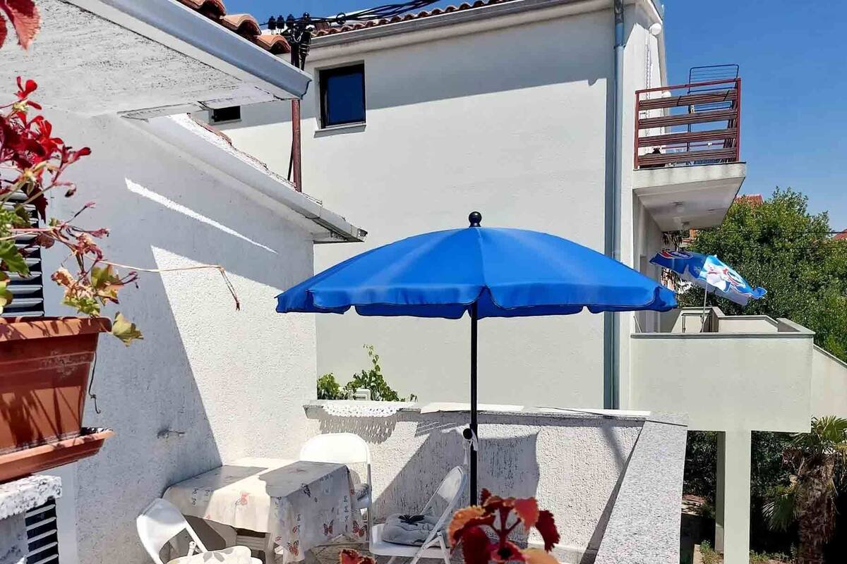 A terrace with a blue umbrella, white chairs, and a table.