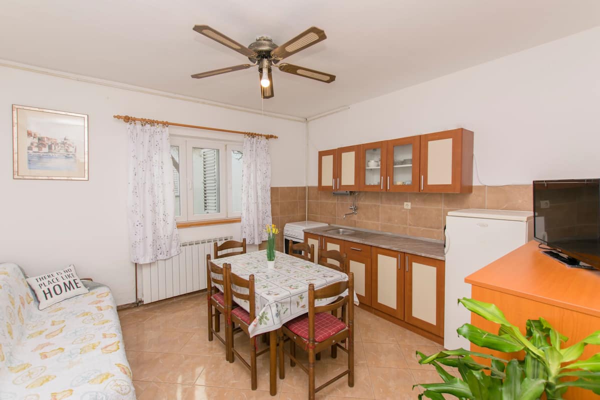 A compact kitchen with a dining table, chairs, a ceiling fan, a refrigerator, and wooden cabinets.