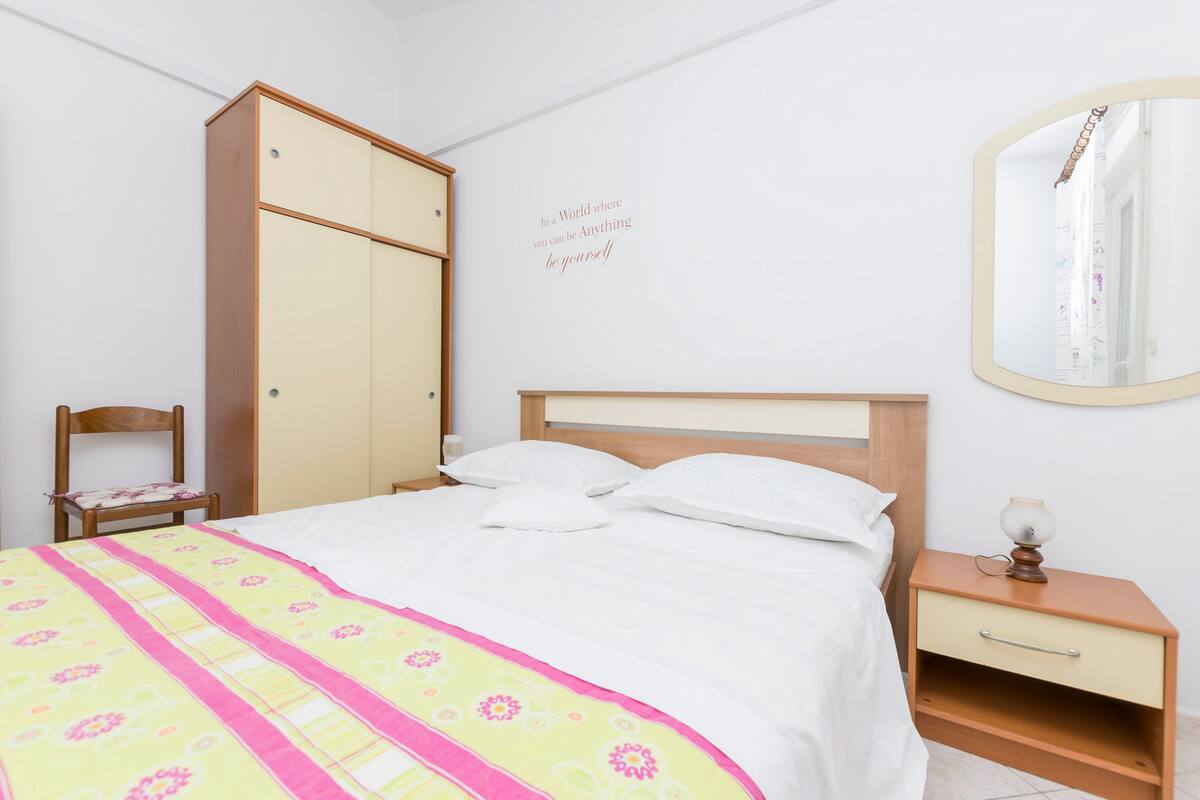 A neatly arranged bedroom with a bed, a wardrobe, a bedside table, and a mirror.