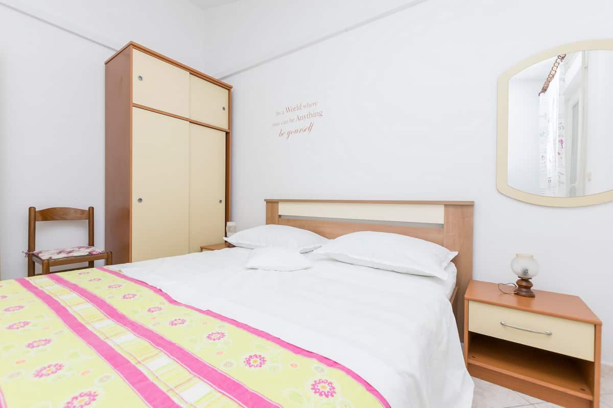 A neatly arranged bedroom with a bed, a wardrobe, a bedside table, and a mirror.