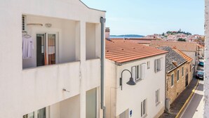 A narrow street with buildings featuring red-tiled roofs and a white building with a balcony. - Apartment Jelena (Primosten)