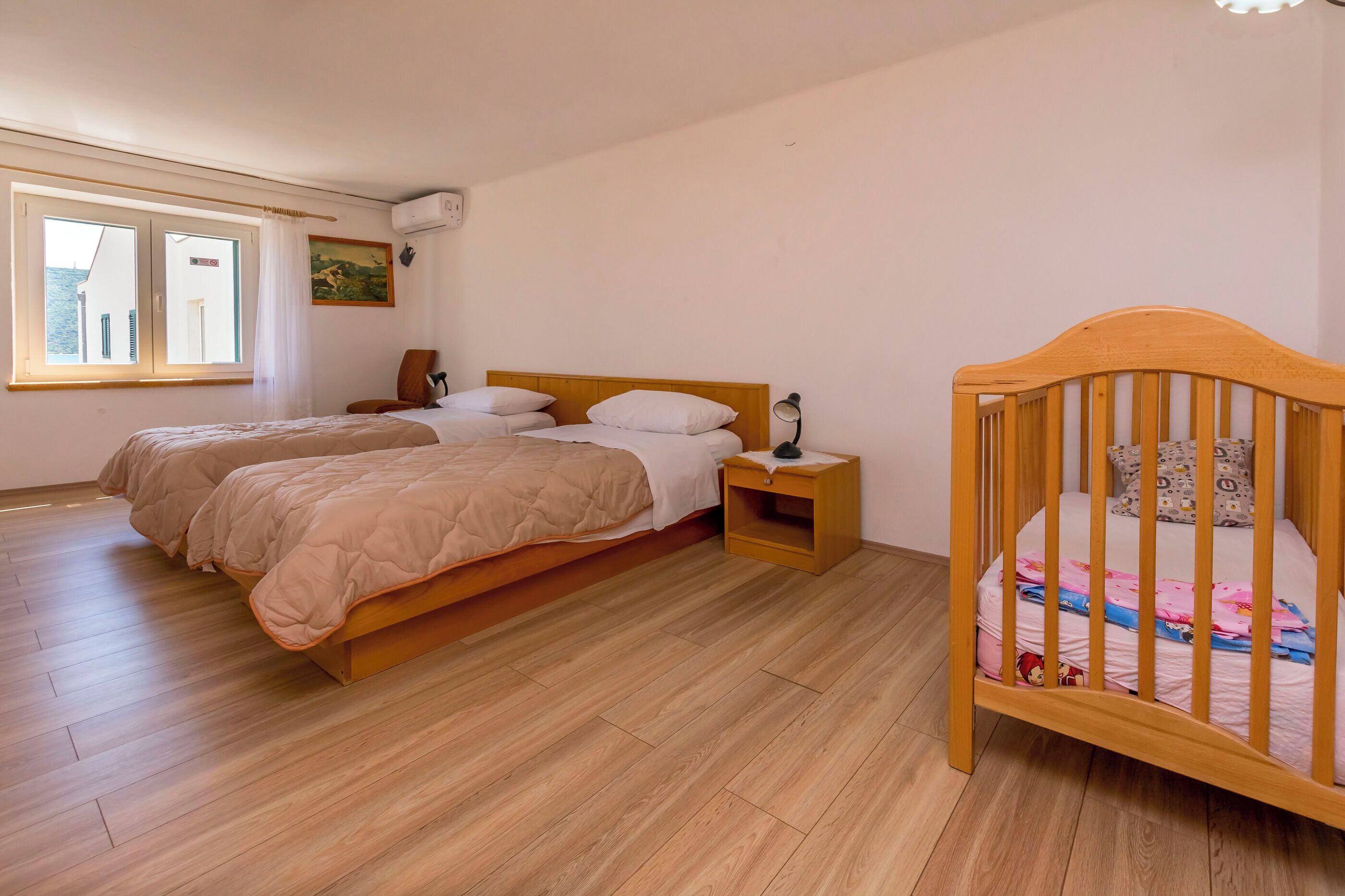 Ein Schlafzimmer mit zwei Betten, einem Holckrippenbett, einem Nachttisch und einem Fenster mit Vorhängen.