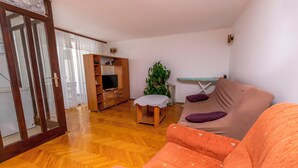 A living room with a wooden floor, a sofa, a television, a small table, and a plant. - Apartment Jelena (Primosten)
