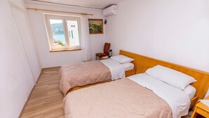 A room with two beds, a wooden floor, a window with a view, and a painting on the wall. - Apartment Jelena (Primosten)