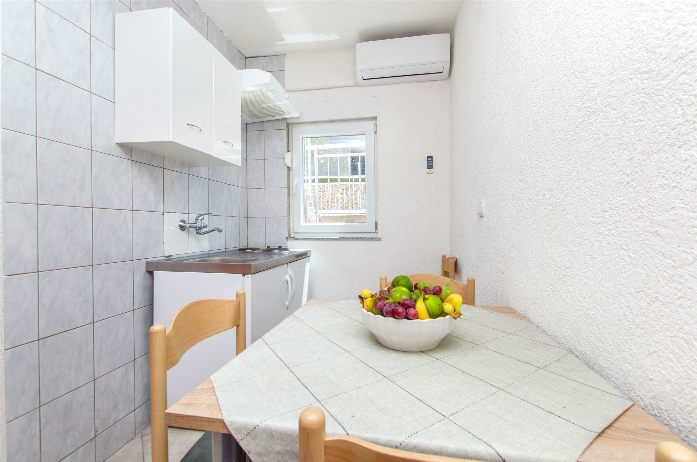 A compact kitchen with a window, a sink, and a bowl of fruit on the table.