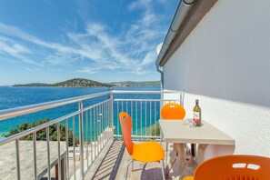 A balcony with a view of the sea, two orange chairs, a table, and a bottle of wine. - Apartments Na Obali Mora (Rogoznica)
