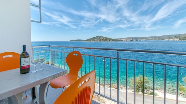 Un balcon avec une table et des chaises, donnant sur une mer turquoise et une île lointaine.