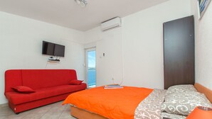 Une chambre à coucher avec un lit, un canapé rouge, une télévision et un appareil de climatisation.