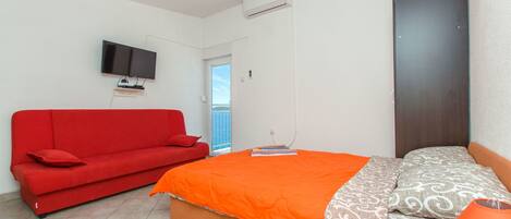 Ein Schlafzimmer mit einem Bett, einem roten Sofa, einem Fernseher und einer Klimaanlage.