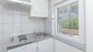 Une cuisine moderne dotée d’une cuisinière à gaz intégrée, d’un évier en acier inoxydable et d’une fen être donnant sur un mur de pierres et de la verdure.