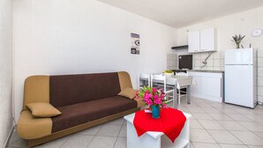 Un salon moderne comprenant un canapé, une table à manger et un coin cuisine avec des placards et un réfrigérateur.