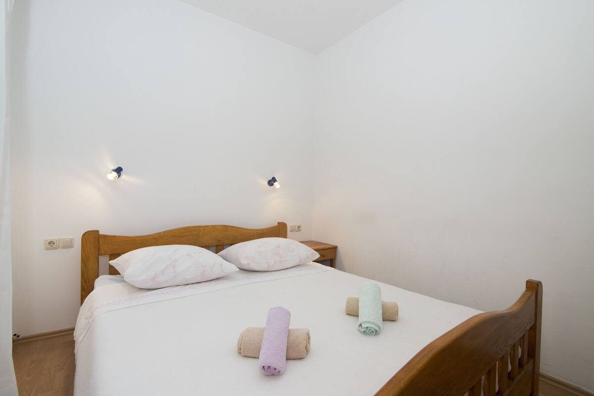 A single bed with a wooden headboard, two wall-mounted light fixtures, and three rolled towels on the bed.
