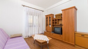 A room with a purple sofa, a wooden cabinet with shelves, a television, and a table with a white tablecloth. - Apartments Jaksa (Jelsa)