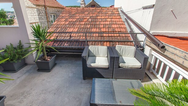 A rooftop terrace with a red-tiled roof, wicker furniture, and potted plants. - Apartments Jaksa (Jelsa)