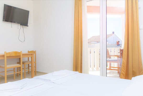 A hotel room with a bed, a desk, a chair, a television, and a sliding glass door to the outside. - Apartments Tiho i Pave (Rogoznica)