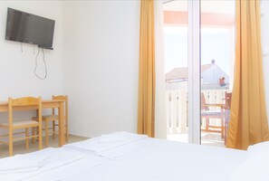 A hotel room with a bed, a desk, a chair, a television, and a sliding glass door to the outside. - Apartments Tiho i Pave (Rogoznica)