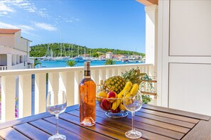 Un balcon avec une table en bois, une bouteille de vin rosé, un panier de fruits et deux verres à vin.