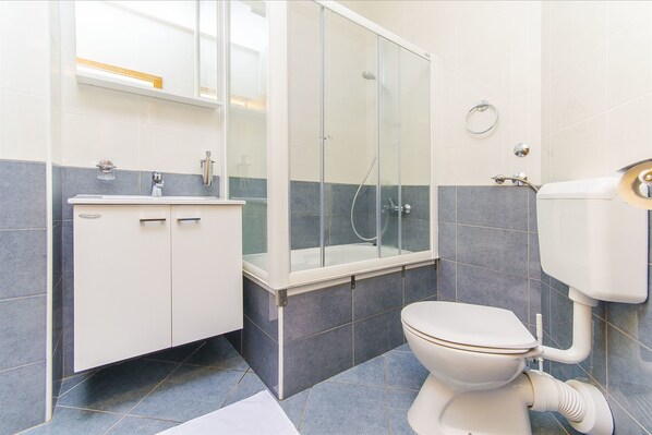 Une salle de bain avec une douche à parois de verre, des toilettes blanches et un lavabo avec un miroir au-dessus.