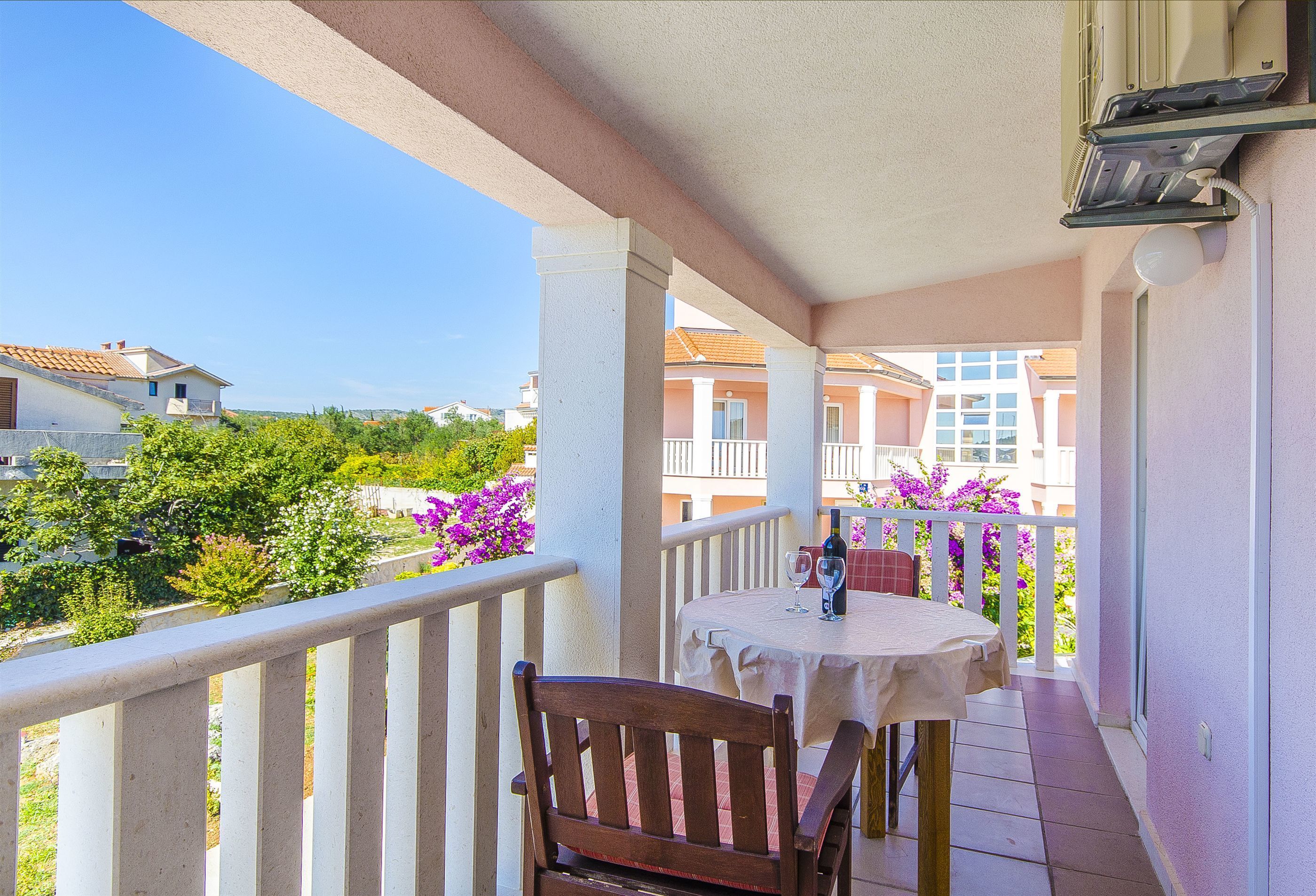 A balcony with a table and chair, overlooking a residential area with houses and greenery.