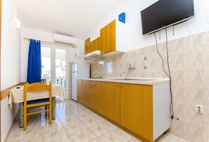 A kitchen with wooden cabinets, a sink, and a television mounted on the wall. - Apartments Tiho i Pave (Rogoznica)