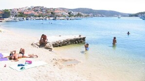 Une plage où l’on peut voir des gens se prélasser au soleil et nager, une digue rocheuse et, au loin, une ville.