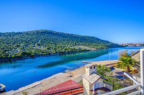 A coastal view with a river, a beach, and a hill with greenery. - Apartments Nada (Rogoznica)