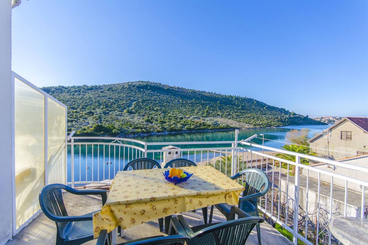 A balcony with a table and chairs overlooking a lake and hills.