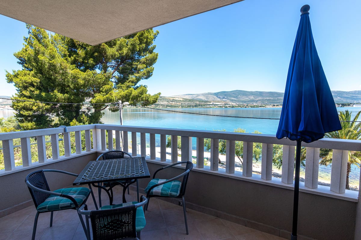 A balcony with a table and chairs, overlooking a body of water and a distant landscape.