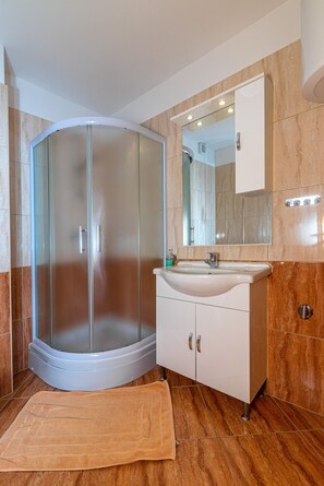 Een moderne badkamer met een douchecabine van glas, een wit wastafelmeubel en een wand betegeld met marmer.