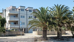 Un immeuble résidentiel à plusieurs étages, doté de balcons, d’un palmier et d’un mur en pierre.
