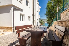 Een houten bank en tafel in een binnenplaats met stenen muren en een wit gebouw.