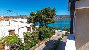 Un quartier résidentiel situé sur la côte, offrant une vue dégagée sur la mer, avec un grand arbre et une rue menant à un bâtiment blanc doté d’un balcon.