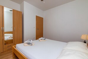 Een slaapkamer met een houten garderobe, een bed met witte lakens en een bedlampje.