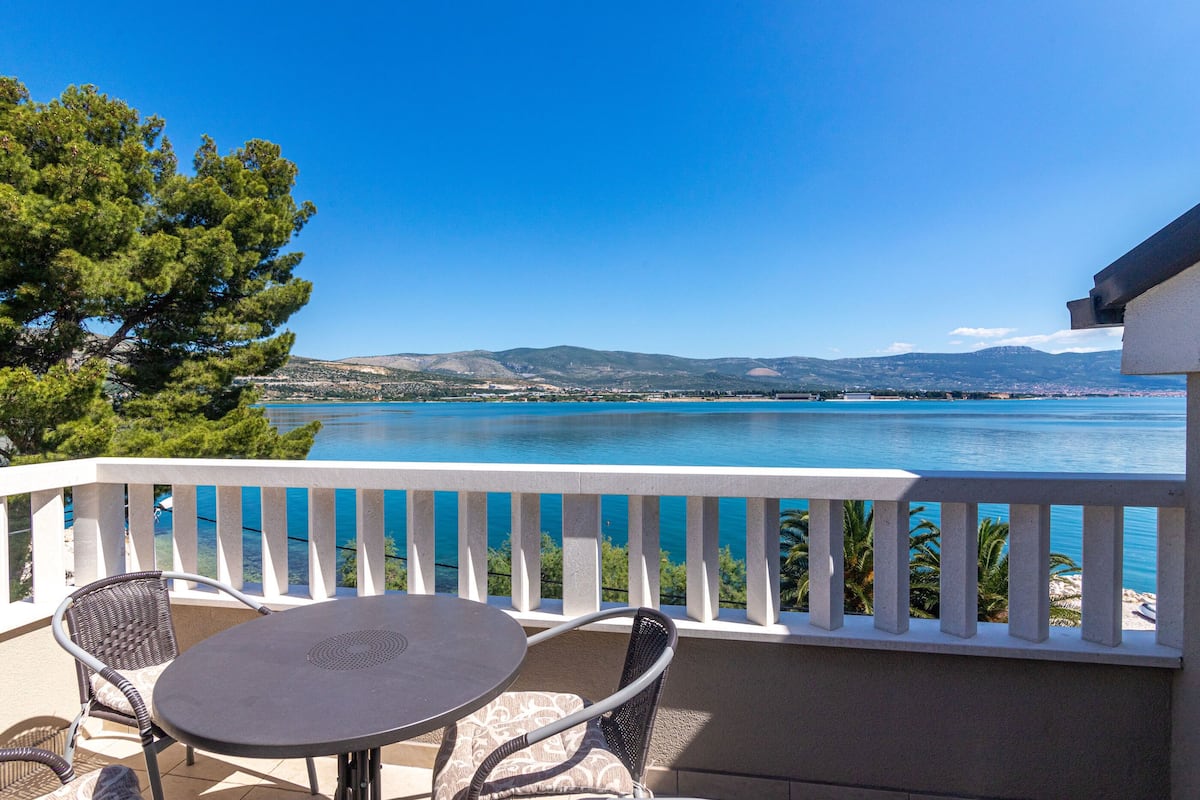 A balcony with a table and chairs overlooking a body of water and distant mountains.