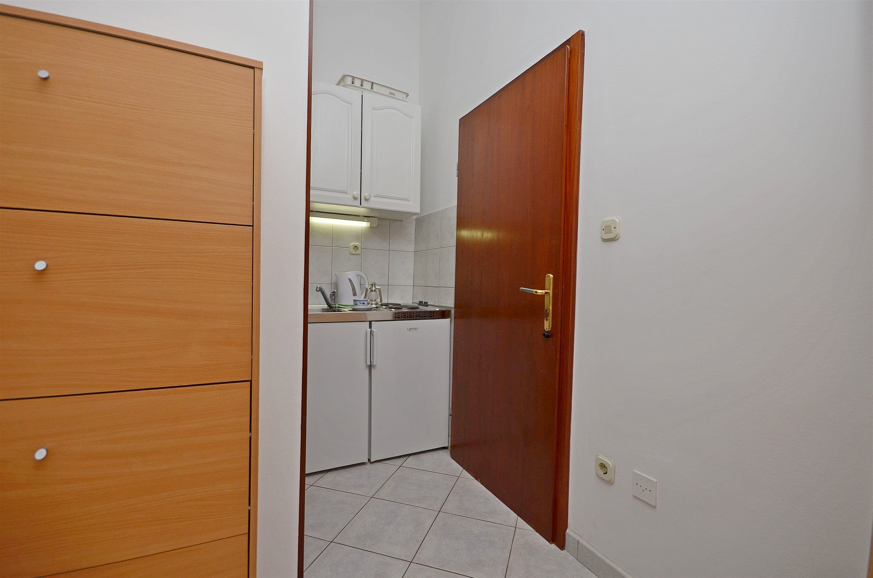 Una piccola cucina con mobili in legno, un piano di lavoro bianco e una porta che dà su un'altra stanza.