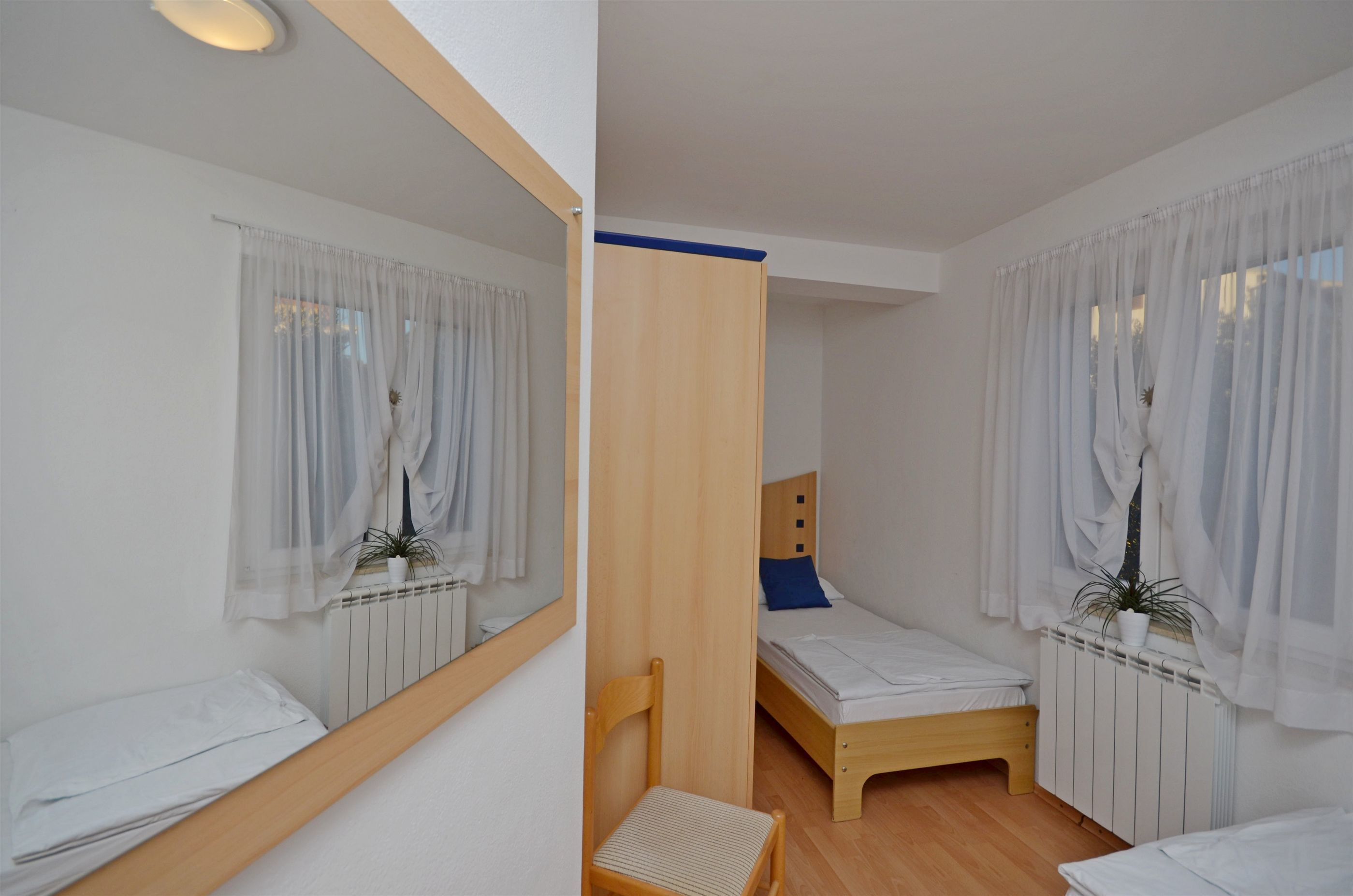 A compact bedroom with two single beds, a wooden chair, a small table, and a mirror.
