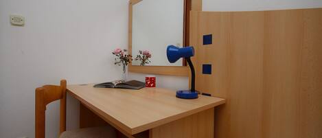 A wooden desk with a mirror, a blue lamp, a red mug, and a book.