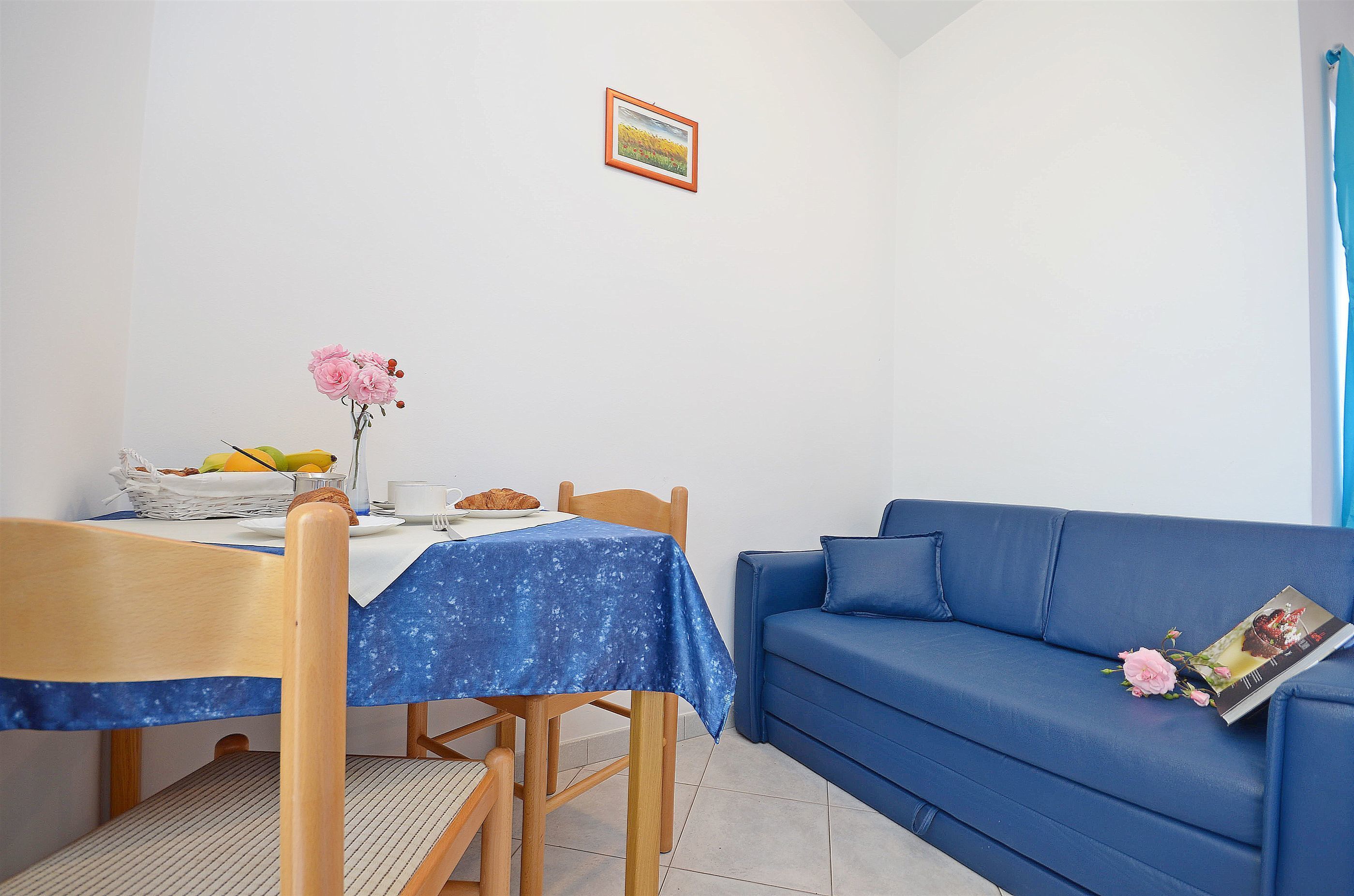 Une petite pièce bien éclairée, avec une table à manger, un canapé bleu et un tableau encadré au mur.