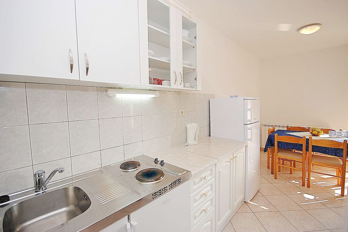 A compact kitchen with white cabinets, a stainless steel sink, a built-in oven, and a dining area with a table and chairs.