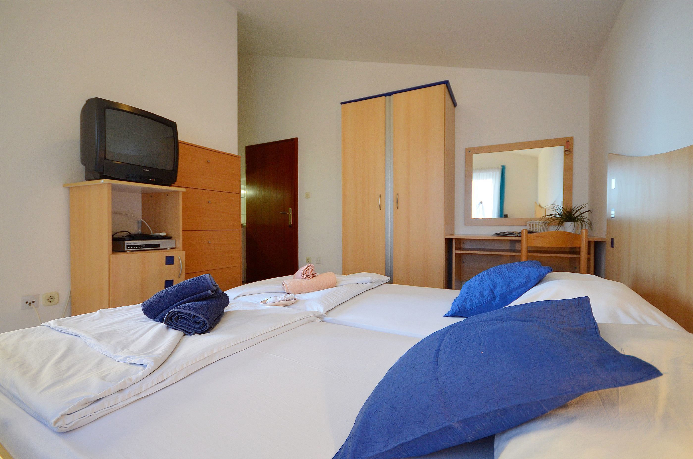 A hotel room with two beds, a television on a wooden cabinet, a mirror, and a desk with a chair.