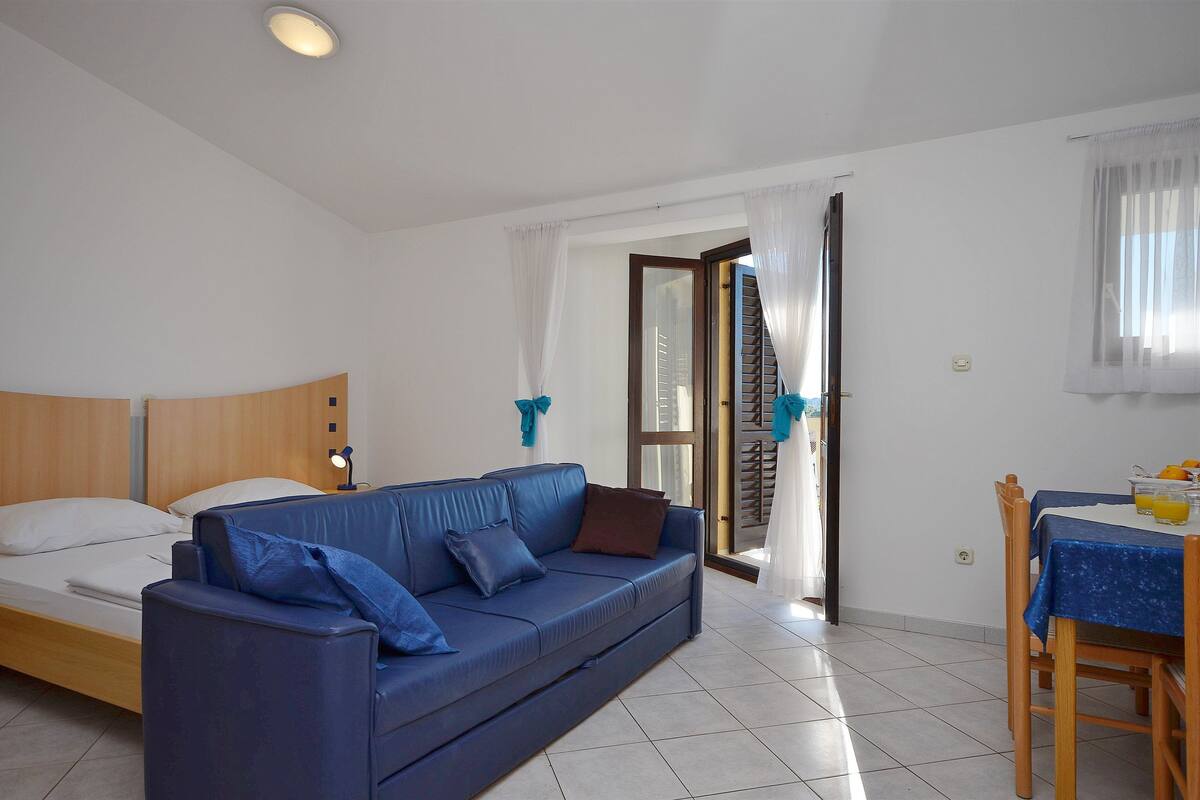 A room with a bed, a blue sofa, a dining table with chairs, and a window with curtains.