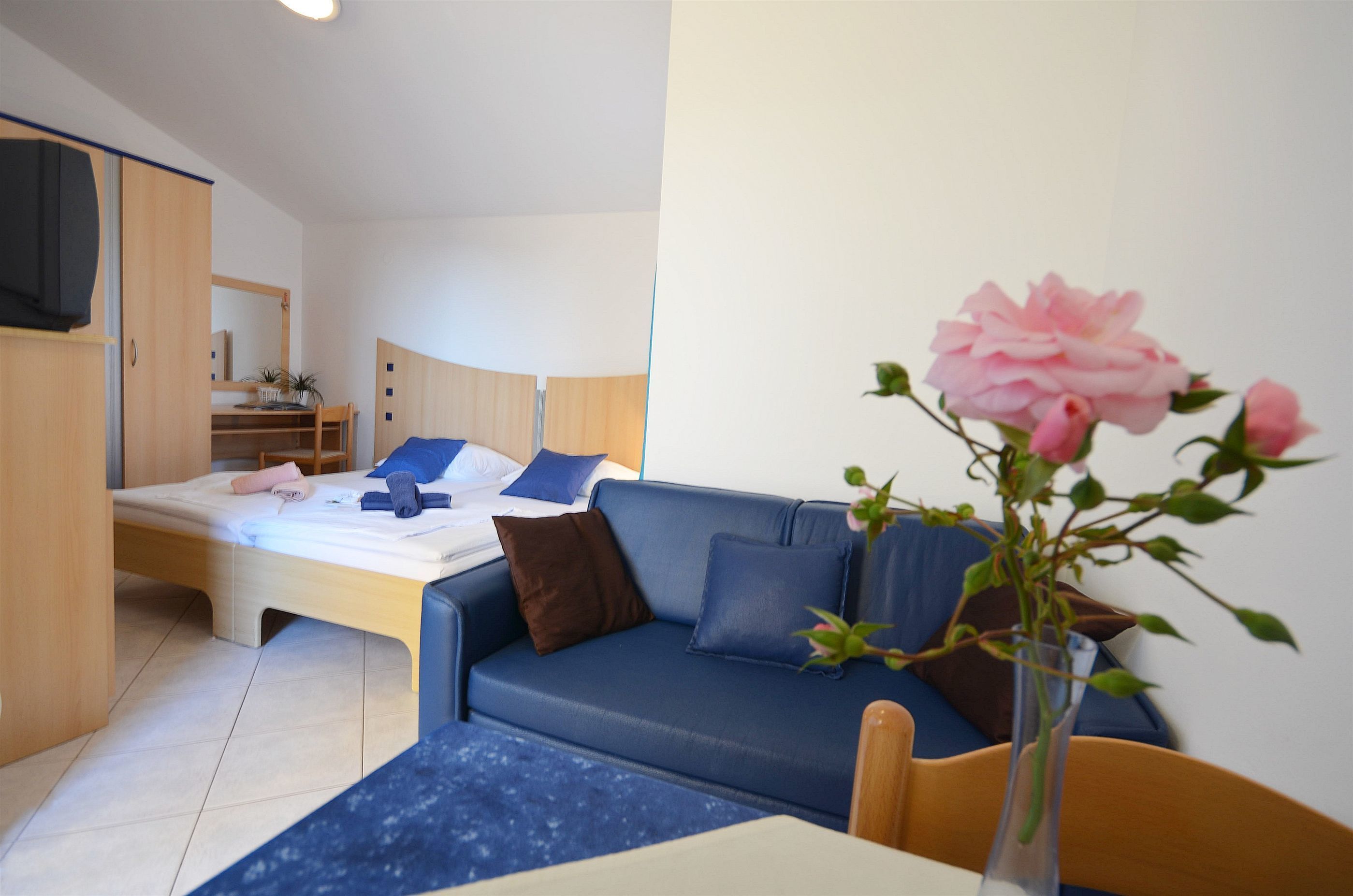 A modern hotel room with a bed, a blue sofa, a small table, and a vase with flowers.