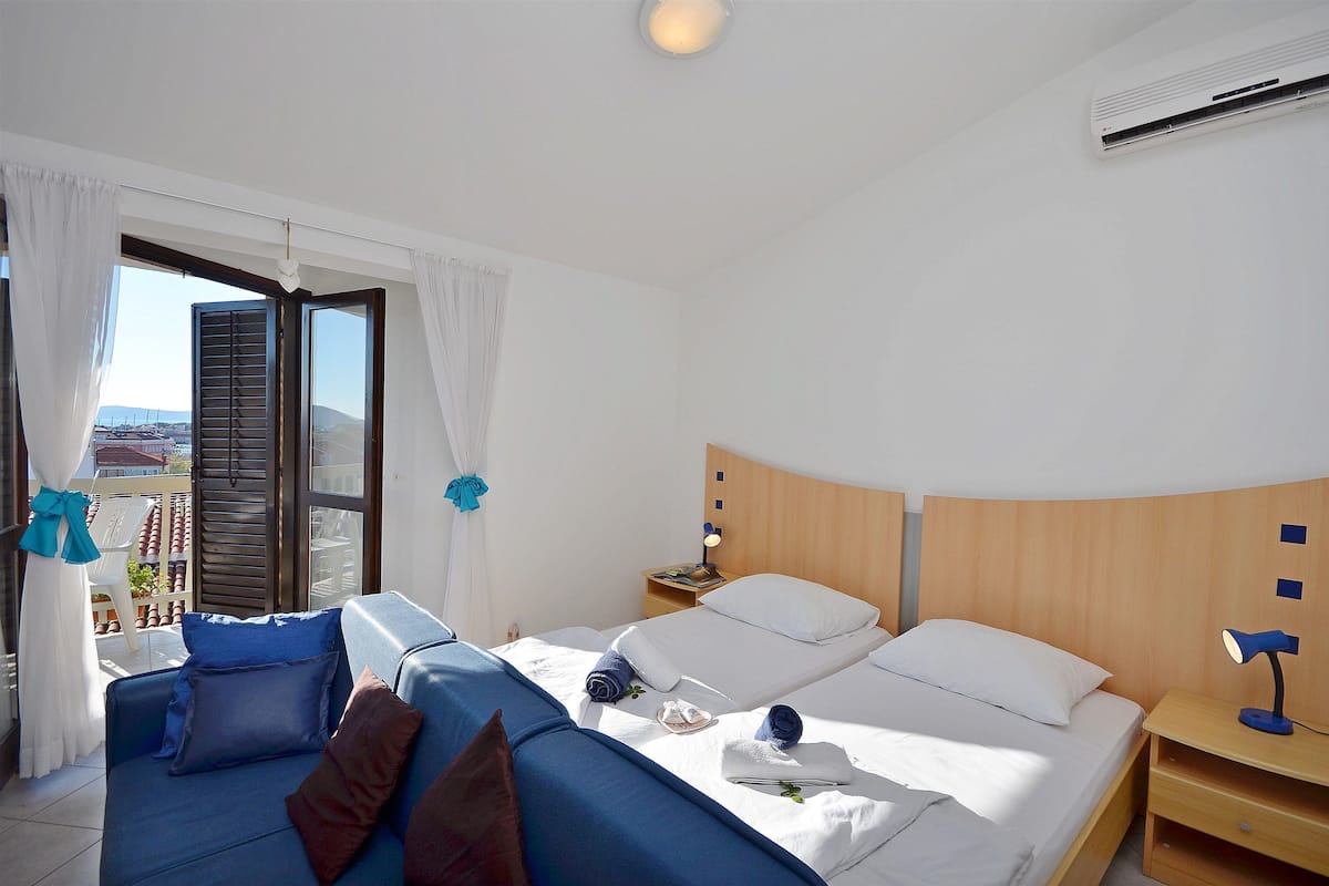 A hotel room with two beds, a sofa, a nightstand, and a balcony with a view.