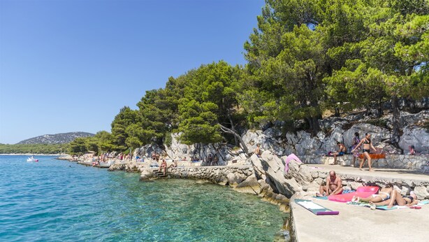 A coastal area with clear water, rocky cliffs, and trees. - Apartments Mira (Tribunj)