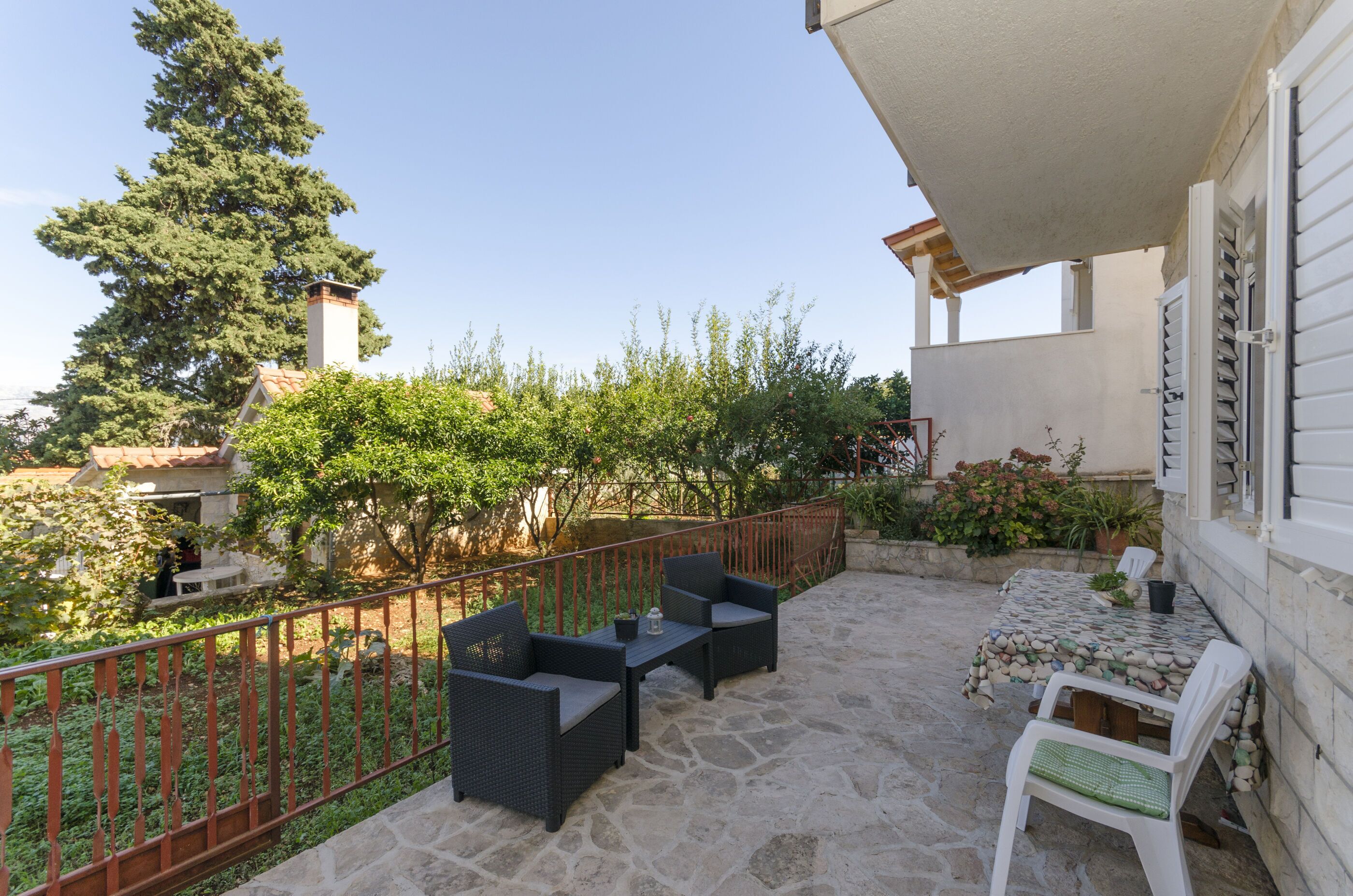 An outdoor patio with stone flooring, a metal railing, and a table with chairs.
