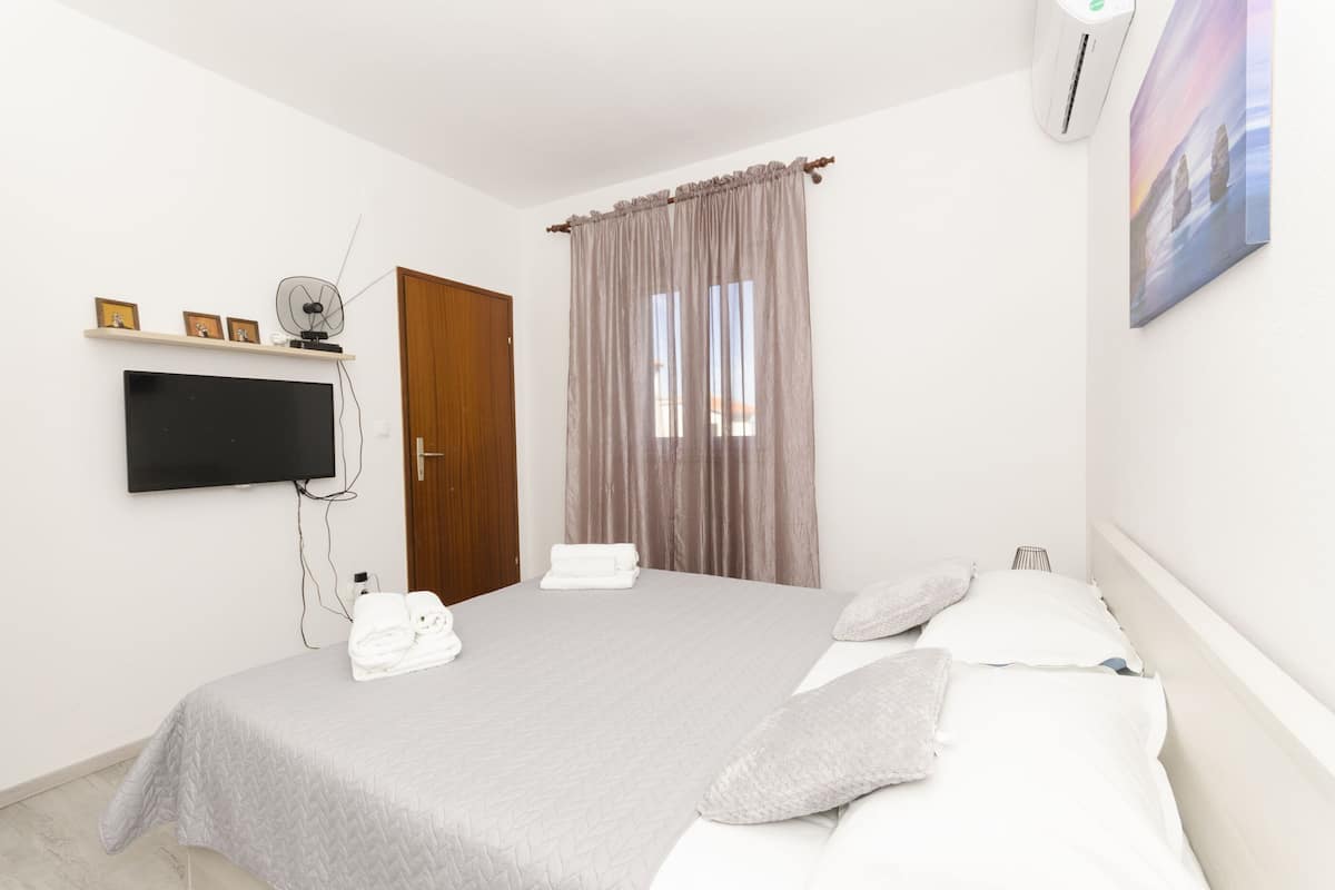 A bedroom with a bed, a TV mounted on the wall, a door, and a window with curtains.