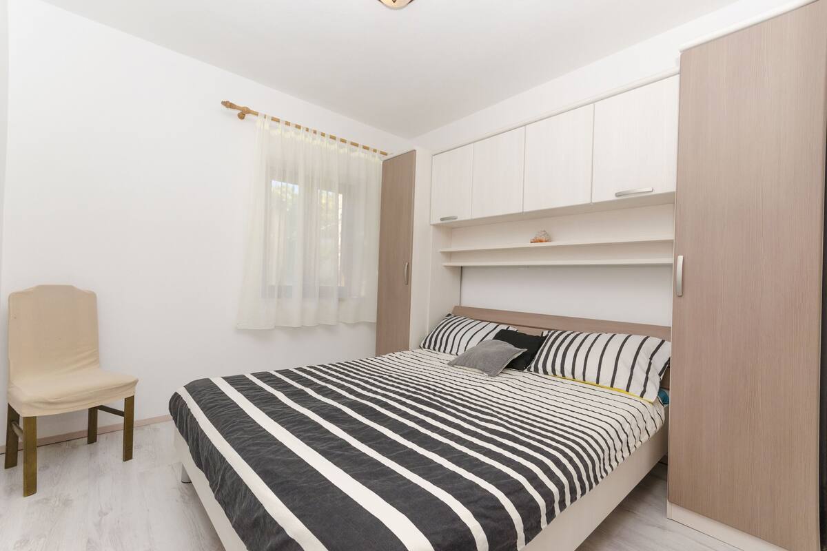 A bedroom with a bed, a chair, a wardrobe, and a window with curtains.