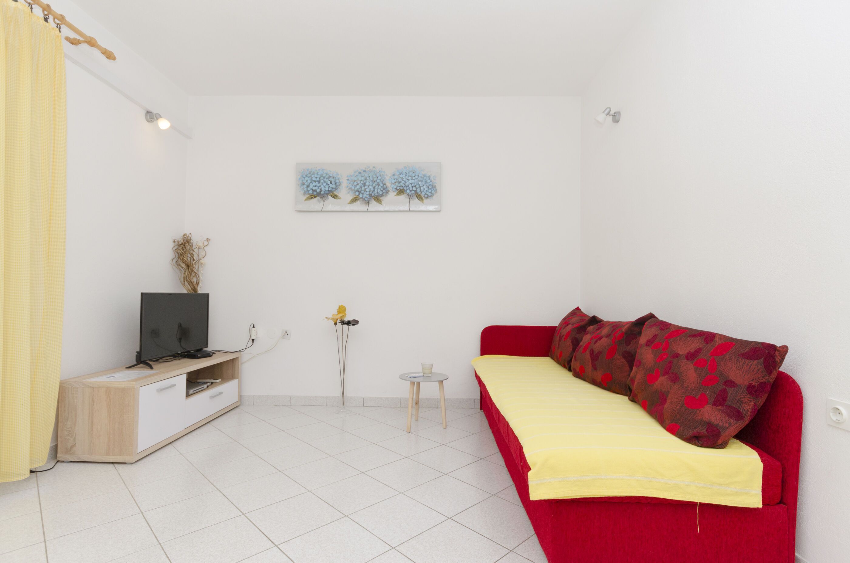 Une petite pièce lumineuse, avec un canapé rouge, un meuble TV en bois et une petite table.