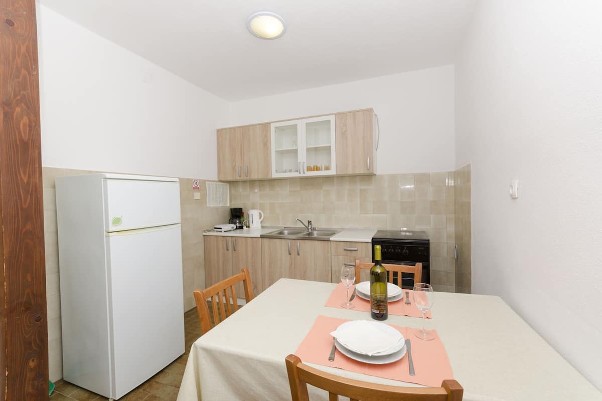 A compact kitchen with a refrigerator, sink, and stove. A dining table with chairs and a wine bottle is set up for a meal.