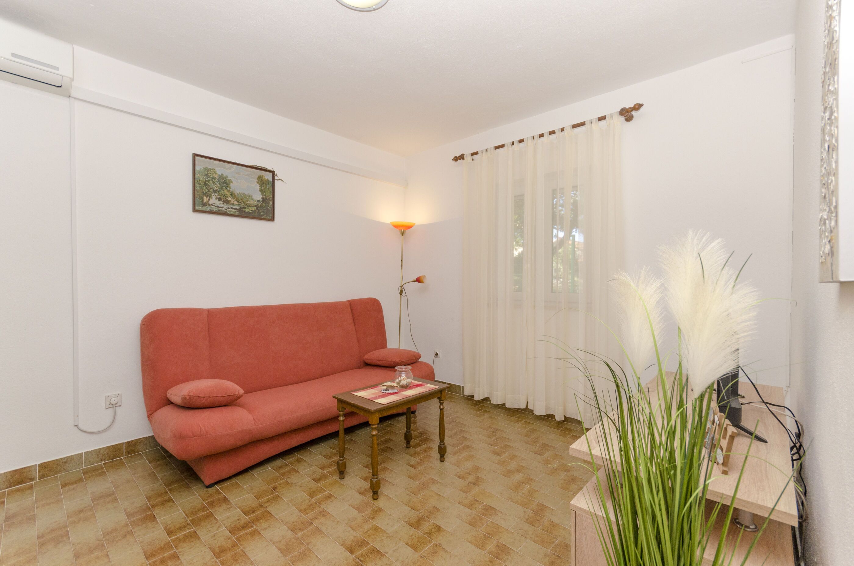 Uma sala de estar com um sofá vermelho, uma mesa de madeira pequena, um abajur e um vaso com planta.